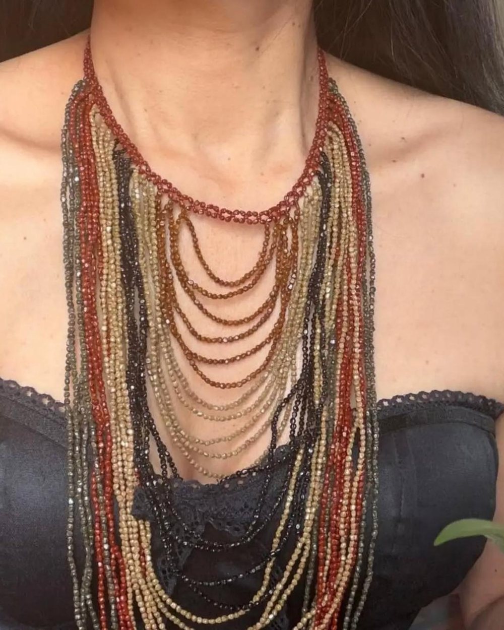 Collar de cascada con muchos hilos de semillas en rojo óxido, arena, mostaza y negro, que cae desde el cuello hasta el pecho.